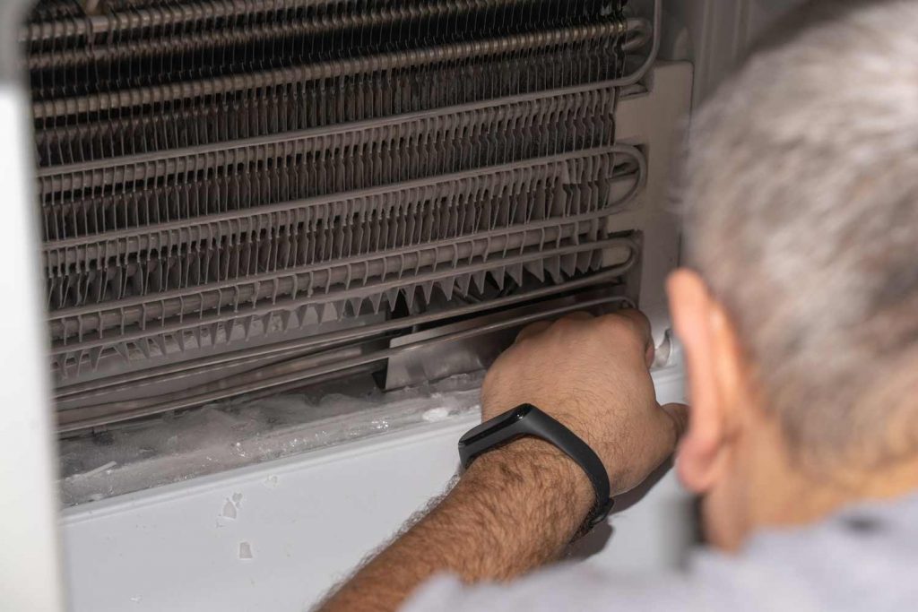 Technician inspecting ice buildup on a freezer's evaporator coils.